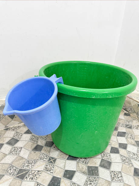 Stock photo showing close-up view of plastic bucket and jug, on bathroom white and grey mosaic tiled flooring, used as a way to clean whilst conserving water.