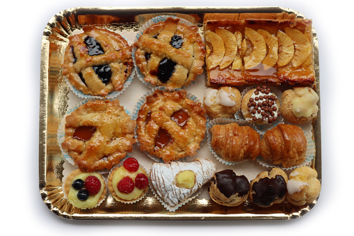 Traditional assortment of italian pastries on golden tray. Cannoli, Babà, cream puffs, small pies with jam, mini tart with cream and fruits and apple pie