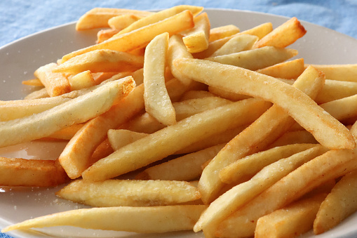 Stock photo showing close-up, elevated view of French fries seasoned with salt on white plate.
