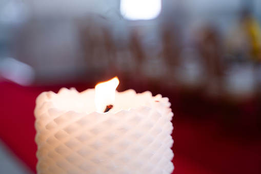 Short white candle on bokeh light background.