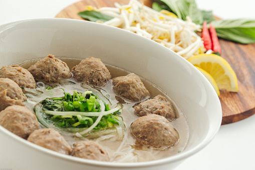 Vietnamese beef meatballs pho noodle soup with veggie side dish on white background