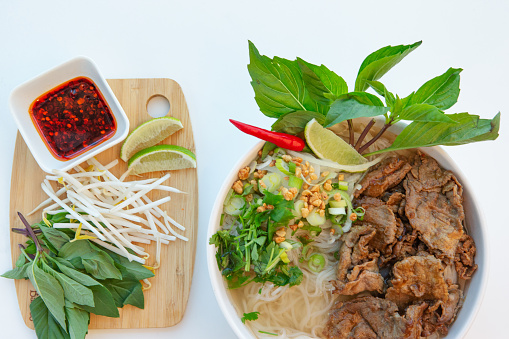 Vietnamese satay beef pho noodle soup with veggie side dish on white background