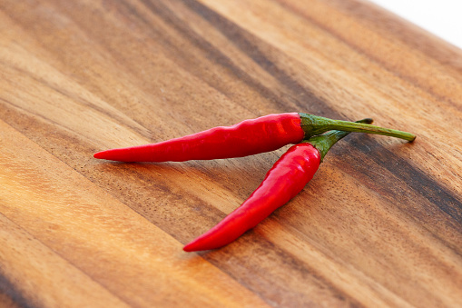 Two whole red chillies peppers on brown wooden cutting board