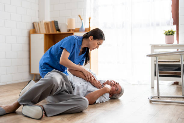 asian caregiver helping senior male from falling on the ground at home. elderly older patient having an accident after doing physical therapy then rescued by attractive therapist nurse in living room. - falling senior adult people one person stock-fotos und bilder