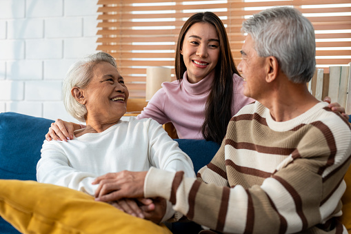 Asian lovely family, young daughter talking and sit with senior parent. Attractive woman granddaughter visit elder old mature couple in house enjoy spend leisure time together in living room and smile