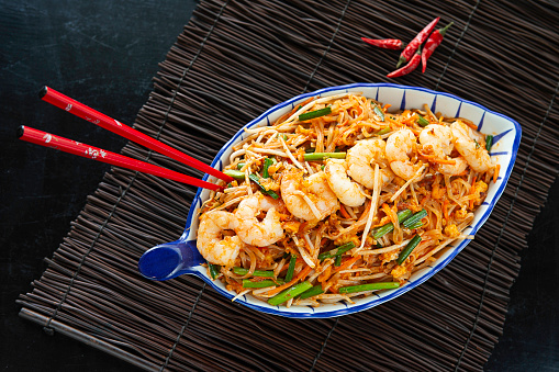 Restaurant prawn rice noodle with bean sprout stir-fried in blue plate with red chopstick on black place mat