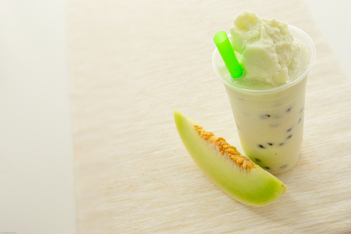 Asian fresh real fruit honeydew melon smoothie in disposable cup on cream table runner