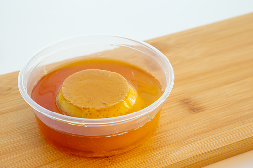 Vietnamese creme caramel pudding in to go plastic container on wooden cutting board