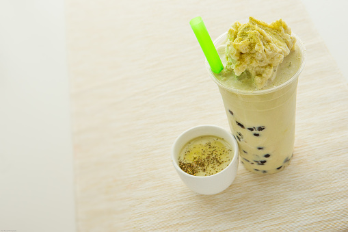 Iced green tea with milk froth on top in glass with ice on table in coffee shop