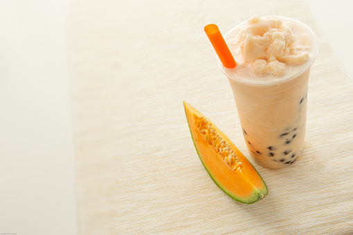 Asian fresh real fruit melon smoothie in disposable cup on cream table runner