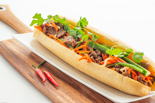 Vietnamese satay beef baguette  with variety of veggie on wooden cutting board on white background