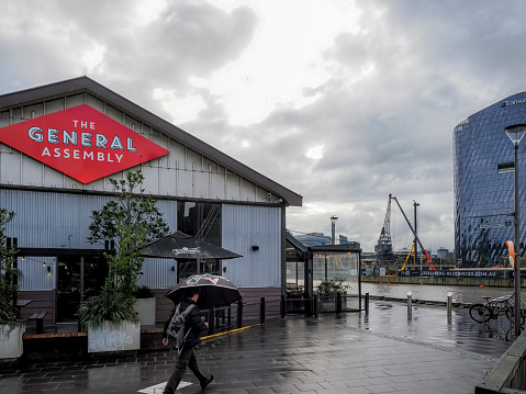 Melbourne, Australia - Aug 30, 2022: South Wharf Promenade beside Yarra River. The General Assembly restaurant on left. A man with umbrella walks by in the rain. Dramatic sky.