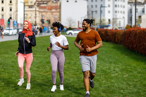 Young African Couple and Their Muslim Female Friend with Hijab are Running Through the City.