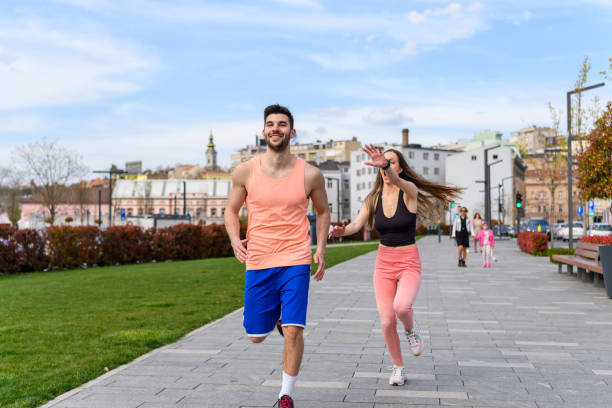 Fit young couple running together outdoors on a grassy area in an urban environment, wearing sportswear and smiling, representing healthy lifestyle, fitness, exercise, and an active outdoor routine