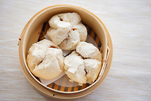 Above view of steamed BBQ pork bun in bamboo steamer on beige table cloth