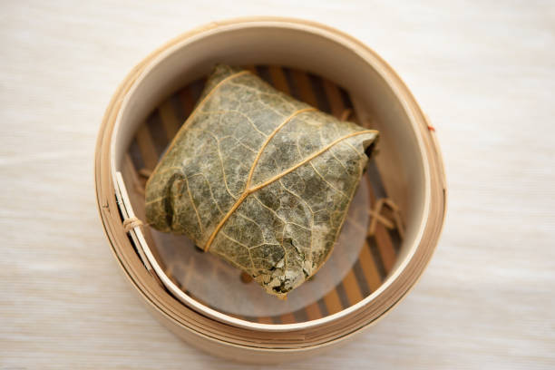 Above view of steamed sticky rice filled with Pork, chicken, sausage and mushrooms wrapped in a lotus leaf. in bamboo steamer on beige table runner