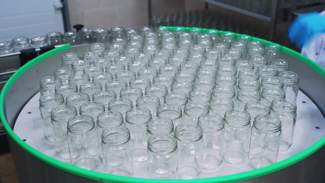 Glass jars are fed onto a conveyor belt at a food factory. Baby food factory, dairy factory, milk or yogurt bottling shop. Glass jars move to an automatic product filling line.