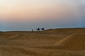 Silhouette of camels in the desert with people at sunrise