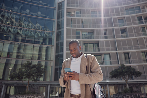 Black man in city with phone, networking and buildings with business chat on morning travel to office. Smartphone, communication and urban businessman consulting on mobile app, walking and typing.