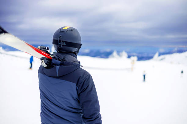Standing in his ski attire, a young adult gazes into the distance, soaking in the serene beauty of the snow-covered mountains around him, his posture capturing the quiet before the exhilarating rush of skiing