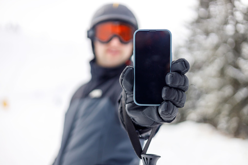 A young adult in ski gear uses his mobile phone on the slopes, a scene that speaks to the modern skier's love for both the adrenaline of downhill skiing and sharing those moments through technology