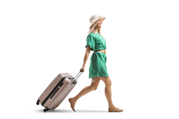 istock Young woman in a green dress walking and pulling a suitcase 1959596422