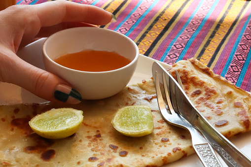 Stock photo showing close-up view of a light, healthy breakfast consisting of a folded crepe with lemon wedges and a white ramekin of honey.