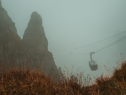 Lost in the ethereal embrace of mist, the mountains reveal their enigmatic beauty from above the veils, as the cable car navigates through this dreamy landscape.