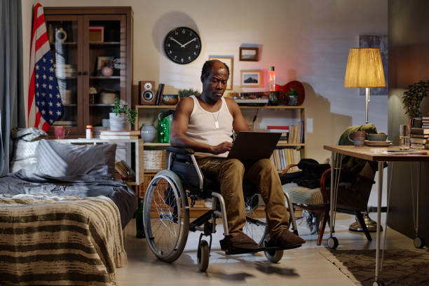 istock Black Man in Wheelchair Looking Through Information on Laptop Screen 1959607743