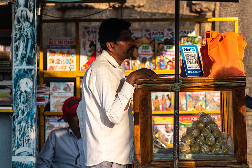 Belur, Karnataka, India - January 9 2023: An Indian street vendor with a paytm upi QR code for payments at his colorful snack stall.