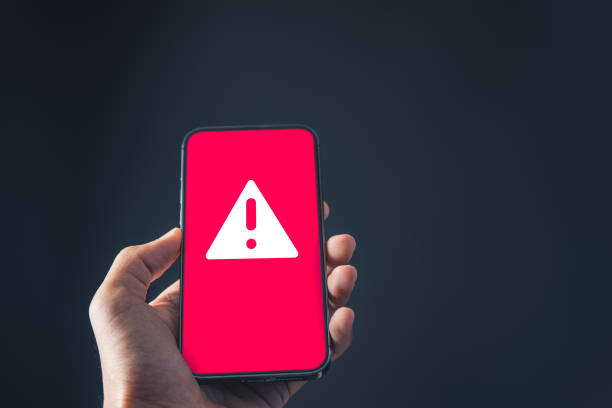 istock Businessman holding mobile phone with red warning alert system hacked screen. System alert for virus,spam,scam and phishing. Cyber security, data security system concept. 1959617991