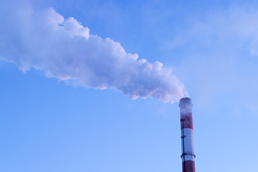 Thick smoke from a chimney on the background of a blue sky close-up