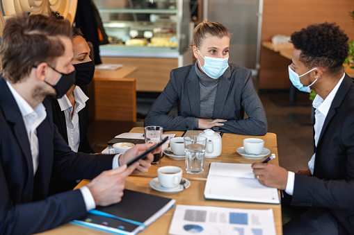 Diverse business people wearing protective face masks and collaborating on their important business project. Business partners having a meeting in a cafeteria.
