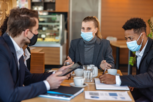 Diverse business people wearing protective face masks and collaborating on their important business project. Business partners having a meeting in a cafeteria.