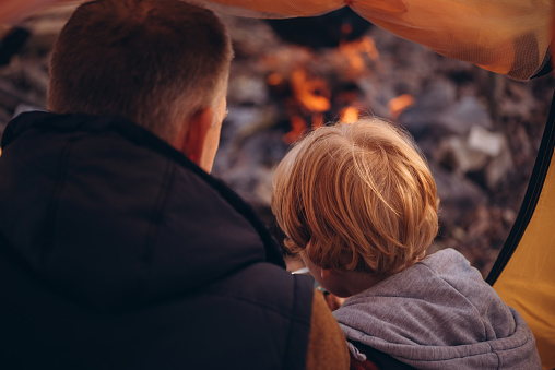 Man and boy tourists autumn time leisure, vacation hiking or traveling touristic activity. Family camping, father and little son relax in forest camp at fire.