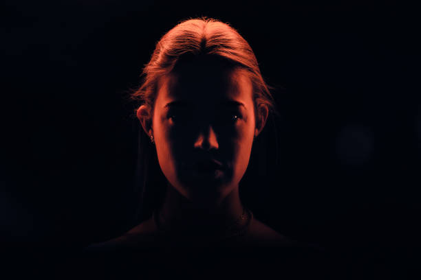 jeune belle femme avec ses cheveux attachés regardant droit dans la caméra éclairée en lumière rouge - silhouette contre jour photos et images de collection