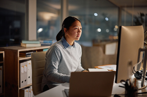 Asian businesswoman, laptop and office at night for working, project management and online for research. Lawyer, computer or connection at desk for focus or reading email on corporate news in company