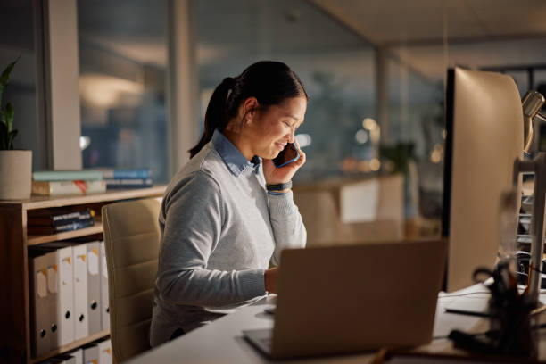 istock Woman, phone call and computer office at night or dark for project online, communication or deadline. Asian person, smile and digital device as research intern for proposal information, chat or late 1959719573