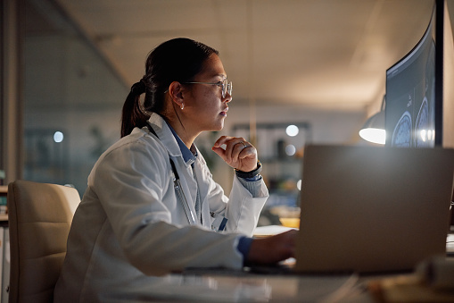 Computer, thinking and doctor asian woman in hospital at night for medical, research or learning. Healthcare, mri scan on screen with young medicine professional in office of clinic for neurology