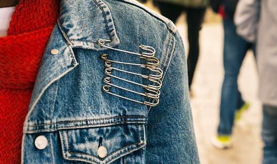 woman with denim jacket and huge safety pins, fashion statement, busy people walking on the sidewalk