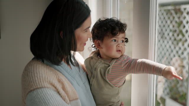 Window, pointing and mother with baby  in living room looking at view for bonding, love and relax. Family, glass and happy mom with child with hand gesture for curiosity, learning and childhood