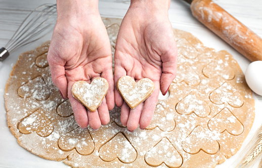 Woman's hands holding two hearts made from dough. Homemade pastry. Cooking process. Close-up. Top view.