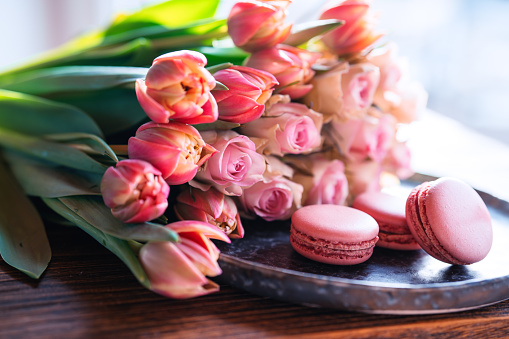 Beautiful pink bouquet of flowers and fine delicacies on dark wood. Sweet pastries with roses and tulips. Concept background for wedding celebrations and mother's day