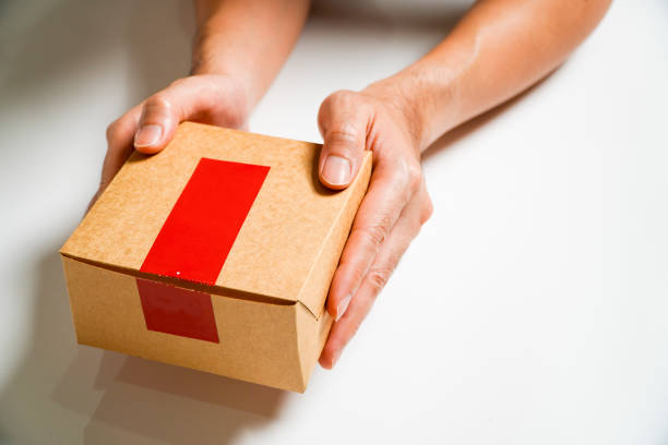 Unrecognizable woman drops off a package at the post office. A female postal worker accepts the package with a smile.