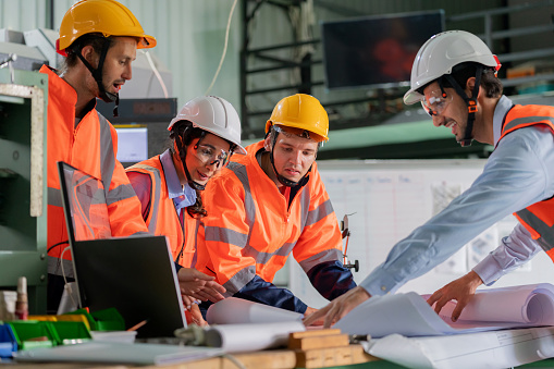 Professionals to a green and eco-friendly future. Engineer in the reflective suit discuss on matters crucial for the energy transition. The engineers are focused, gesturing toward concepts that revolve around renewable energy, solar panels, and sustainable business practices.