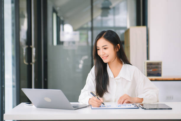 istock Young Asian businesswoman working with working notepad, tablet and laptop documents talking on the smartphone, tablet and laptop video call 1959832676