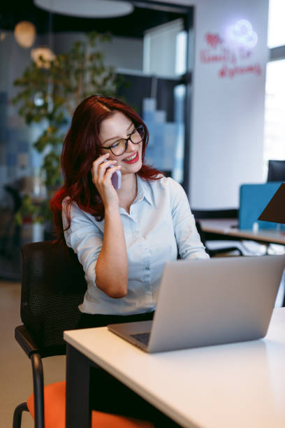 istock Portrait of a young attractive businesswoman enjoying work while using laptop computer and talking phone in an open modern office 1959838019