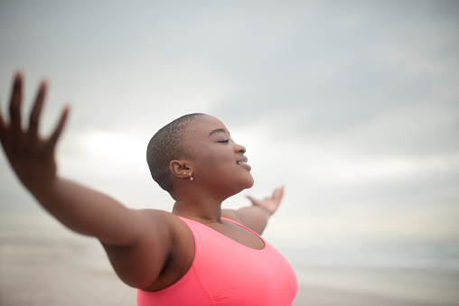 Black woman, freedom and wellness in nature with fitness, health and meditation by outdoor. Young, african person, exercise and open arms in gym clothing, cape town and happy with peace by cloudy sky