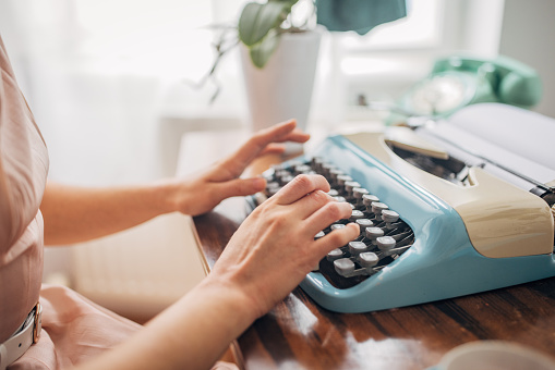 Unrecognizable young woman typing on a typewriter in her apartment.