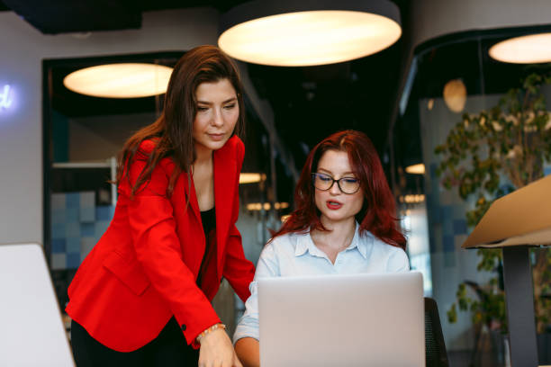 istock Strategic Collaboration: Two Young Business Women Utilizing Digital Tablet and Laptop in a Modern Startup Office. Planning, Strategizing, and Discussing Success as a Team in the Boardroom Meeting 1959848675